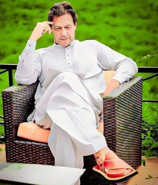Imran Khan seated on a wicker chair outdoors, resting his hand at his temple
