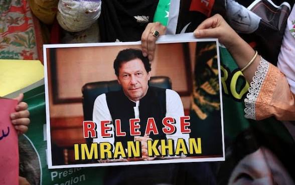 Hands holding a printed protest sign showing Imran Khan and the words Release Imran Khan